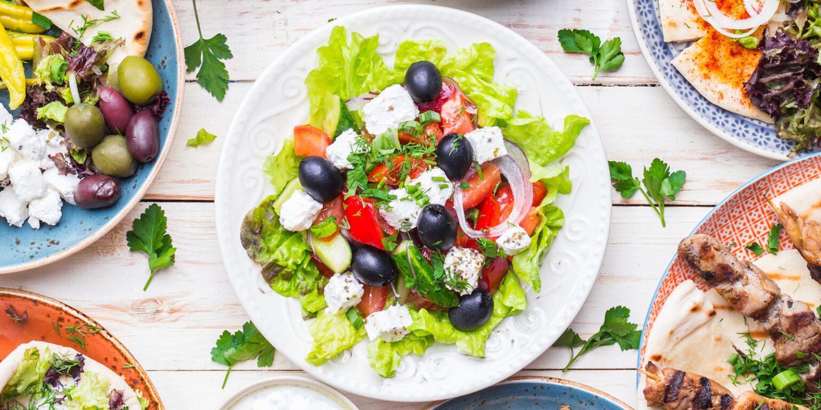 Greek food background. Meze, gyros, souvlaki, fish, pita, greek salad, tzatziki, assortment of feta, olives and vegetables. Traditional different greek dishes set. Top view. Food for share. Close-up